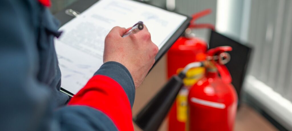 Man writing on clipboard with extinguisher in the background